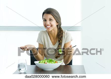 Teen girl eating salad, holding up hand and shrugging shoulders View Large Photo Image Stock Image - Teen girl eating salad, holding up hand and shrugging shoulders. Fotosearch