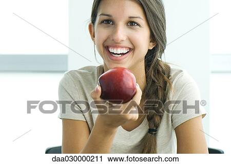 Stock Image - Teen girl holding apple, smiling, portrait. Fotosearch