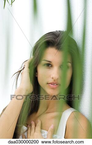 Stock Image - Teen girl looking at camera through foliage, hand on chest. Fotosearch