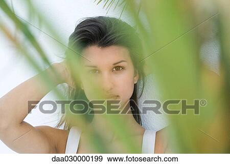 Stock Photo - Teen girl looking at camera through foliage, hands in hair. Fotosearch