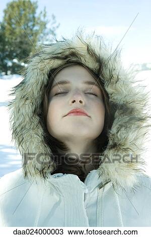 Stock Image - Teen girl wearing parka in snow, eyes closed. Fotosearch