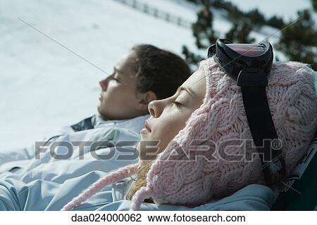 Stock Image - Teen girls sitting in chairs in snowy landscape, relaxing in sun, close-up. Fotosearch