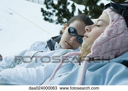 Stock Image - Teen girls sitting in chairs in snowy landscape, relaxing in sun, close-up. Fotosearch