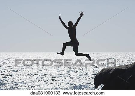 Stock Image - Teenage boy jumping into ocean, silhouette. Fotosearch