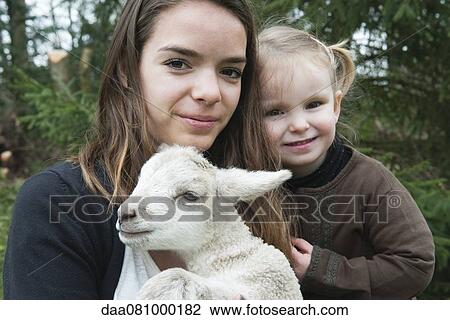 Stock Image - Teenage girl and little sister with pet lamb, portrait. Fotosearch