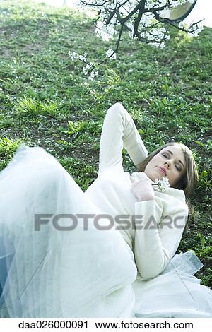Stock Image - Teenage girl lying on the ground with hand behind head, holding flower, eyes closed. Fotosearch