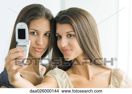 Teenage girl photographing self and twin sister with cell phone, both making faces View Large Photo Image Picture - Teenage girl photographing self and twin sister with cell phone, both making faces. Fotosearch