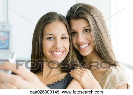 Teenage girl photographing self and twin sister with cell phone, both smiling View Large Photo Image Stock Photography - Teenage girl photographing self and twin sister with cell phone, both smiling. Fotosearch
