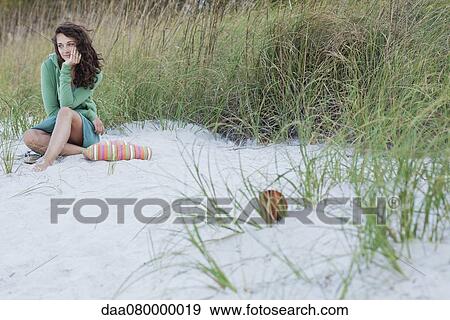 Stock Photo - Teenage girl sitting alone on beach, smiling. Fotosearch