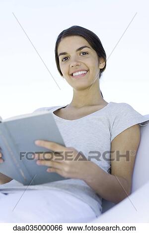 Stock Photograph - Teenage girl sitting, holding book, smiling at camera. Fotosearch