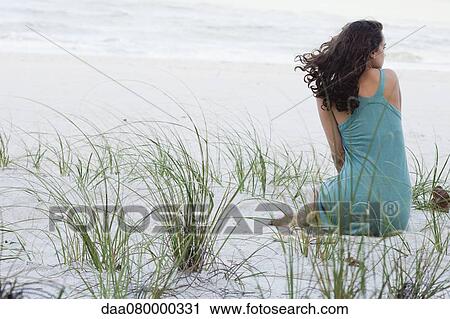Stock Image - Teenage girl sitting on beach, rear view. Fotosearch