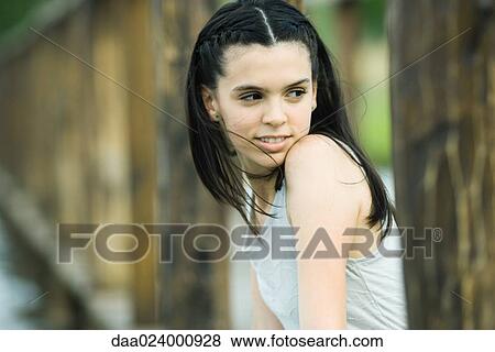 Teenage girl sitting outdoors, looking over shoulder, smiling View Large Photo Image Stock Photo - Teenage girl sitting outdoors, looking over shoulder, smiling. Fotosearch