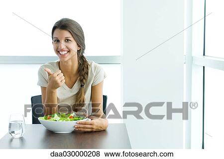 Teenage girl sitting with salad, making thumbs up gesture, smiling at camera View Large Photo Image Stock Photo - Teenage girl sitting with salad, making thumbs up gesture, smiling at camera. Fotosearch