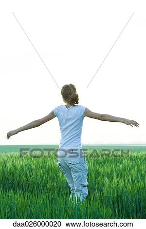 Stock Image - Teenage girl standing in field with arms outstretched, rear view. Fotosearch