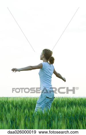 Stock Photo - Teenage girl standing in field with arms outstretched, side view. Fotosearch
