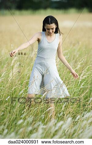 Teenage girl walking in field of tall grass with arms out, looking down View Large Photo Image Stock Image - Teenage girl walking in field of tall grass with arms out, looking down. Fotosearch
