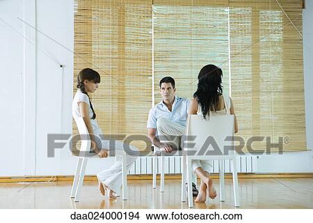 Three adults sitting in chairs, having therapy session, looking serious View Large Photo Image Picture - Three adults sitting in chairs, having therapy session, looking serious. Fotosearch