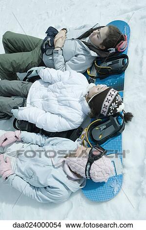 Picture - Three sisters lying on snow with heads resting on snowboard. Fotosearch