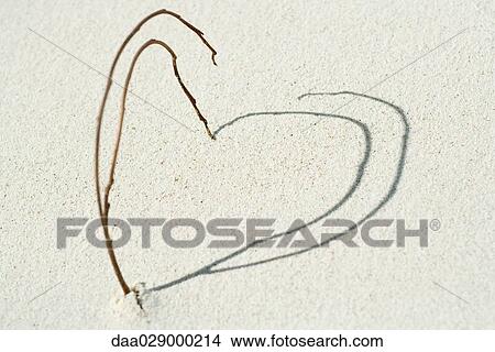 Picture - Twigs and shadows arranged in heart shape on the beach, close-up. Fotosearch
