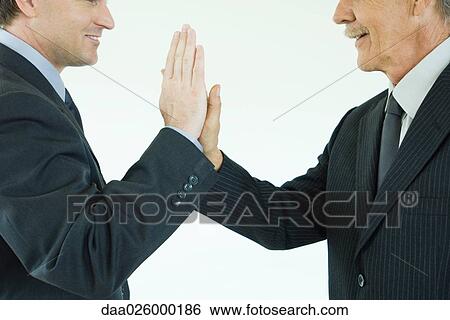 Stock Photograph - Two businessmen giving each other a high-five, cropped side view. Fotosearch