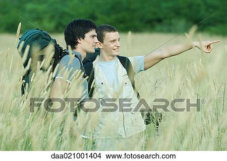 Two hikers standing in field, one pointing out of frame View Large Photo Image Picture - Two hikers standing in field, one pointing out of frame. Fotosearch