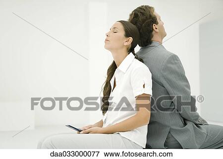 Two professionals sitting back to back, eyes closed, woman holding cell phone View Large Photo Image Stock Photo - Two professionals sitting back to back, eyes closed, woman holding cell phone. Fotosearch