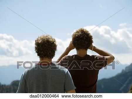 Two young men looking at mountain view with binoculars, rear view View Large Photo Image Picture - Two young men looking at mountain view with binoculars, rear view. Fotosearch