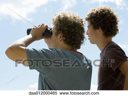 Stock Photography - Two young men looking at view with binoculars, rear view. Fotosearch