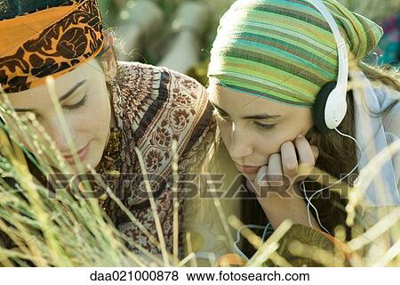 Two young women lying in field, one listening to headphones, close-up View Large Photo Image Stock Photo - Two young women lying in field, one listening to headphones, close-up. Fotosearch
