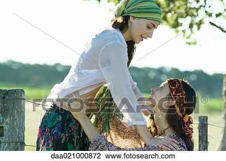 Stock Image - Two young women outdoors, one standing on fence, the other holding her around the waist. Fotosearch