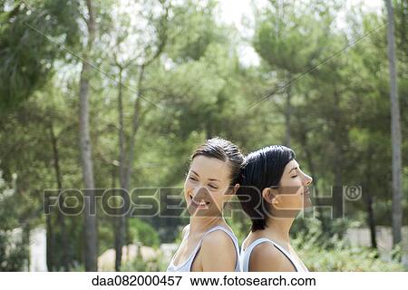 Stock Photo - Two young women sitting back to back outdoors. Fotosearch