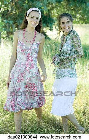 Two young women standing in field, smiling at camera View Large Photo Image Picture - Two young women standing in field, smiling at camera. Fotosearch
