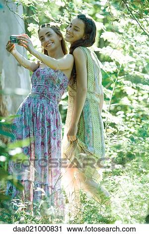 Two young women wearing sundresses, standing in forest, taking photo of selves with digital camera View Large Photo Image Stock Image - Two young women wearing sundresses, standing in forest, taking photo of selves with digital camera. Fotosearch