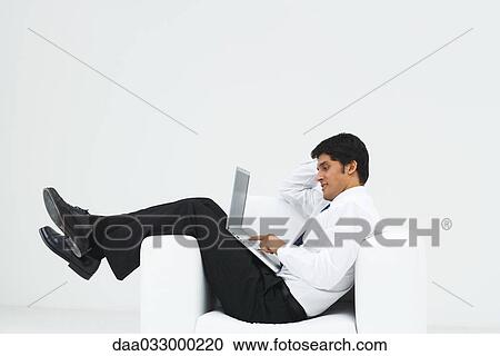 Well-dressed man reclining in armchair, using laptop, side view View Large Photo Image Stock Image - Well-dressed man reclining in armchair, using laptop, side view. Fotosearch