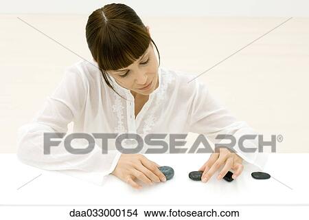 Picture - Woman arranging row of stones, looking down. Fotosearch