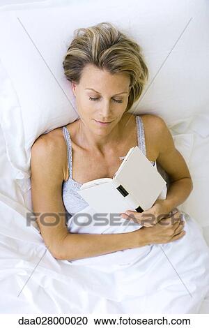 Stock Image - Woman asleep in bed, holding book against chest. Fotosearch