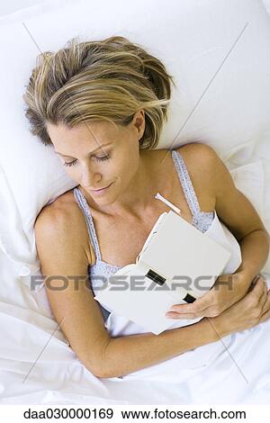 Woman asleep in bed, holding book against chest View Large Photo Image Stock Photo - Woman asleep in bed, holding book against chest. Fotosearch