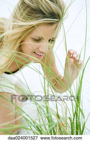 Stock Photo - Woman bending over, looking through grass, close-up. Fotosearch