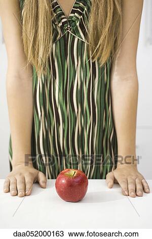 Stock Image - Woman contemplating apple, cropped. Fotosearch