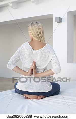 Stock Photo - Woman doing reverse prayer position on bed, rear view. Fotosearch
