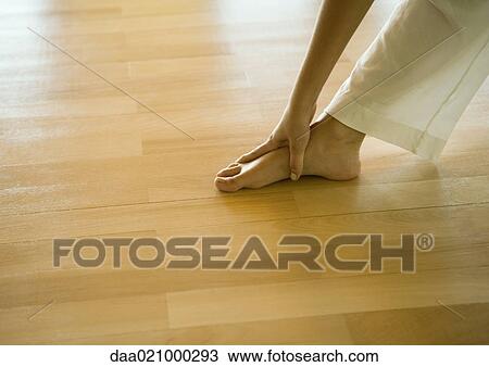 Stock Image - Woman doing standing forward bend, cropped view of hands and feet. Fotosearch