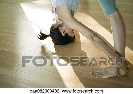 Stock Image - Woman doing standing forward bend yoga pose (Uttanasana). Fotosearch