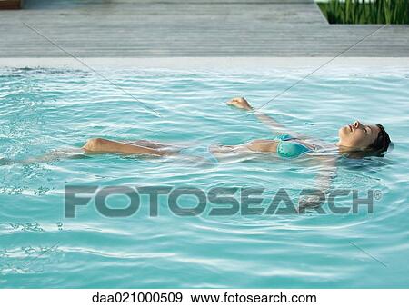 Stock Photo - Woman floating on back in pool, full length. Fotosearch