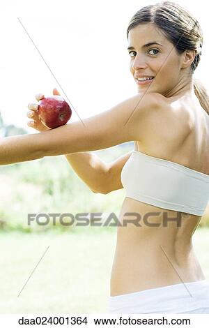 Picture - Woman holding apple on arm, looking over shoulder at camera. Fotosearch