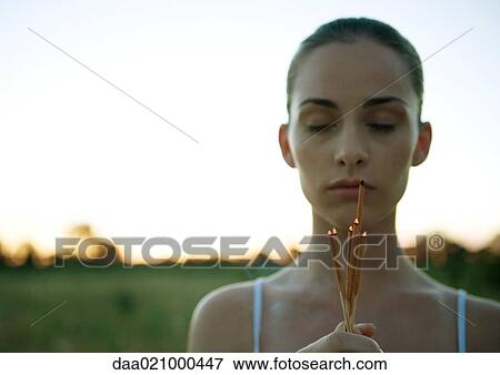 Woman holding bunch of incense, eyes closed, at sunset View Large Photo Image Stock Photo - Woman holding bunch of incense, eyes closed, at sunset. Fotosearch