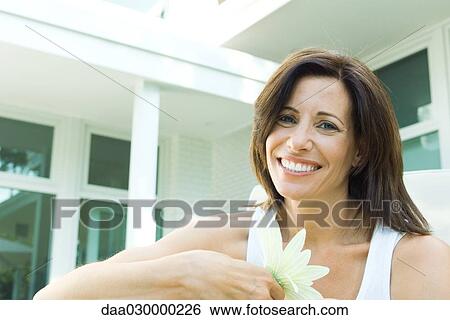 Stock Photograph - Woman holding flower, smiling at camera, portrait. Fotosearch