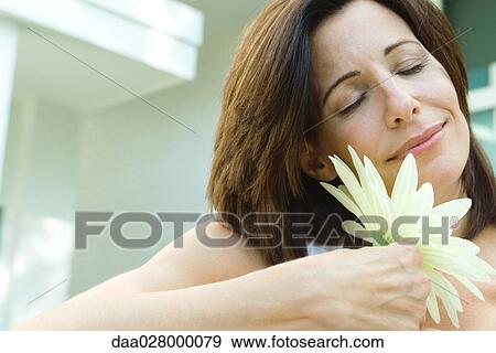 Woman holding flower to face, eyes closed, smiling View Large Photo Image Stock Photo - Woman holding flower to face, eyes closed, smiling. Fotosearch