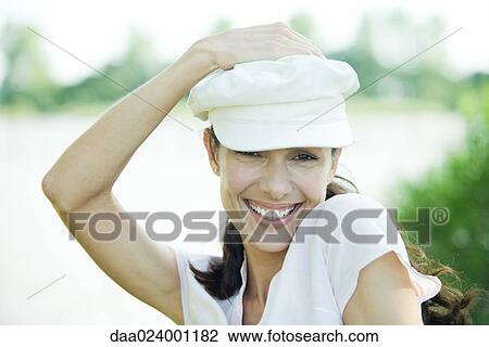 Woman holding hat on head, smiling at camera, portrait View Large Photo Image Stock Image - Woman holding hat on head, smiling at camera, portrait. Fotosearch