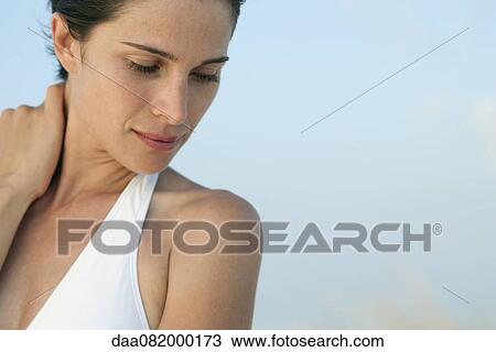 Stock Image - Woman holding neck, looking down, portrait. Fotosearch