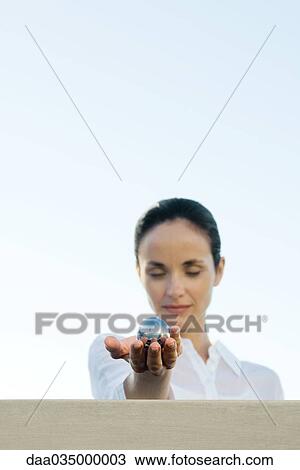 Stock Image - Woman holding out metal sphere, eyes closed. Fotosearch